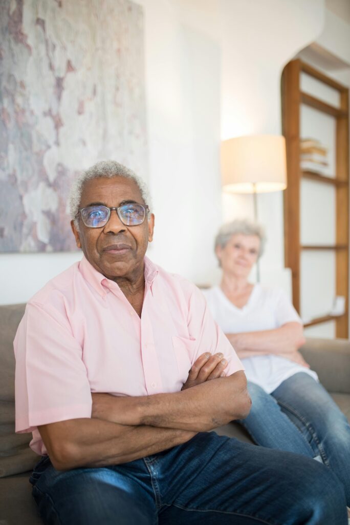 Senior adults relaxing with arms crossed on a couch in a cozy home setting.